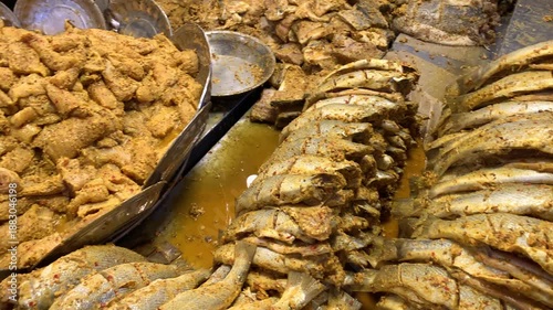 Close-up of fresh whole fish heavily coated in traditional aromatic spices and red chili flakes, prepared and ready for deep frying or grilling at a local market.