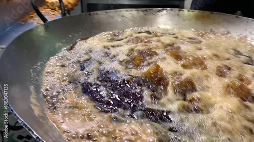 A high-energy, close-up shot of whole seasoned chickens being lowered into and deep-fried in a large vat of bubbling, boiling oil at a street food market.