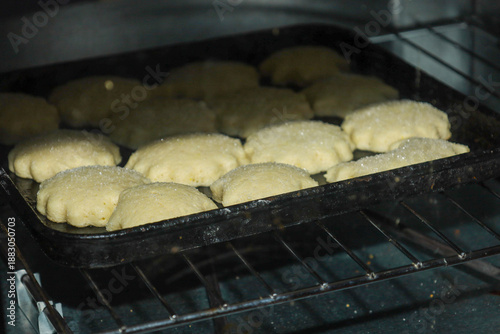Homemade sugar cookies gradually rise on a baking sheet inside a preheated oven, filling the kitchen with a sweet aroma.