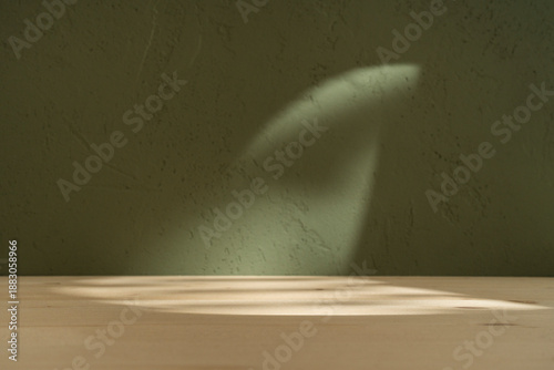 Wood table on boho green wall with sun light and shadows. Product cosmetic background.