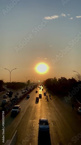 Golden sunset over a busy multi-lane highway with traffic and silhouettes of trees at dusk.