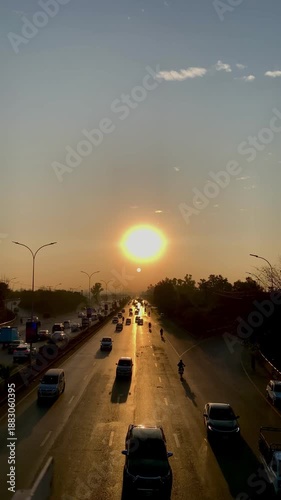 Golden sunset over a busy multi-lane highway with traffic and silhouettes of trees at dusk.