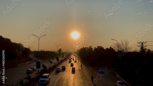 Golden sunset over a busy multi-lane highway with traffic and silhouettes of trees at dusk.
