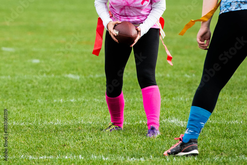 Confident female athlete dressed in pink uniform holding football during high school powder puff game with teenage girls. 