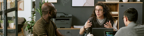 Photography Young adult Caucasian man with long curly hair explaining project to young Black