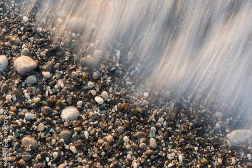 Obraz na plátne Long exposure of sea wave receding over colorful pebble beach