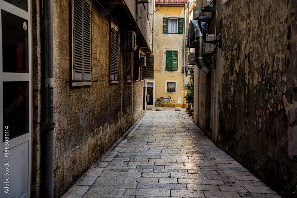 Fototapeta premium Quiet narrow street in the old town of Zadar with a bicycle parked near colorful historic buildings. Mediterranean city atmosphere, urban travel scene and coastal lifestyle in Croatia. 