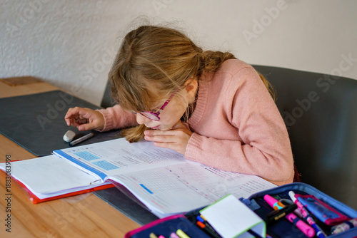 Fotografie Cute elementary school girl writing in her workbook and doing school homework