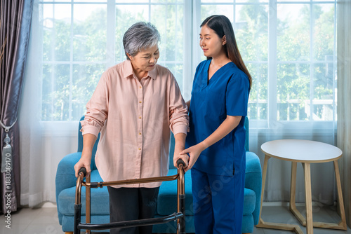 Senior elderly Asian woman using walker assisted by caregiver in nursing home