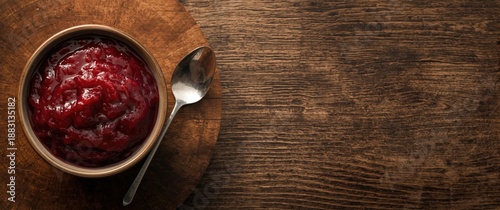 Close-up shot of a bowl and spoon with fresh cranberry sauce on a white wooden surface