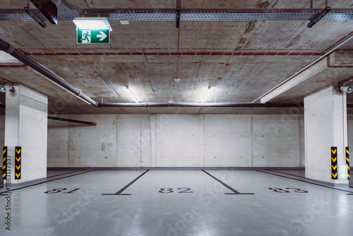 Empty underground parking spaces with concrete walls and emergency exit sign
