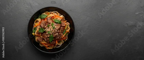 Obraz  z motywem Korean Japchae in a black bowl on a dark slate table, showcasing glass noodles with vegetables and meat, authentic Asian food.