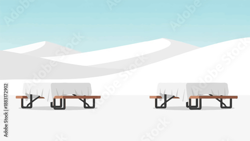 Two empty picnic tables are set up in a snowy landscape under a pale blue sky