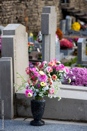 Fotografi Bouquets de fleurs fraiches et multicolore déposés sur les tombes dans cimetière à l'occasion de la Toussaint