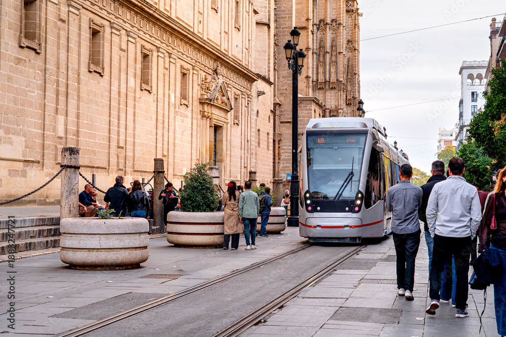 Fototapeta premium Tram is moving in front Cathedral Seville with tourists walking, life on streets Andalusian city. Urban transport in Spain.