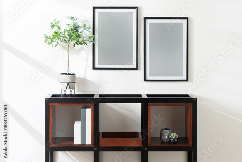 Tableau sur toile Modern, Bright Living Room Interior with Bookshelf, Books, and Vase, Blank Photo Frames Mockup on White Wall, Lit by Natural Light from Side Window