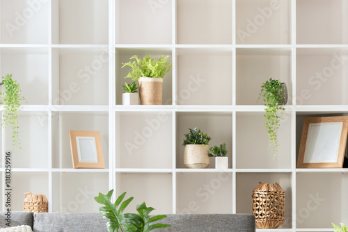 Modern Minimalist Living Room Interior Design Featuring a White Square-Spaced Bookshelf, Grey Sofa, and Plants, Neatly Organized for a Homey Ambience, Illuminated by Natural Light.