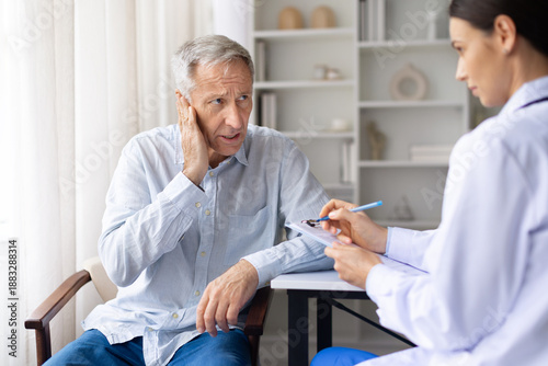 Fotografie Senior male patient reporting ear pain to female doctor during medical visit in