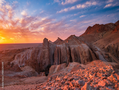 Sunset view over the Chebika oasis in Tunisia, with dramatic rocky cliffs glowing in warm light beneath a colorful sky, highlighting desert beauty, tranquility, and a timeless arid landscape