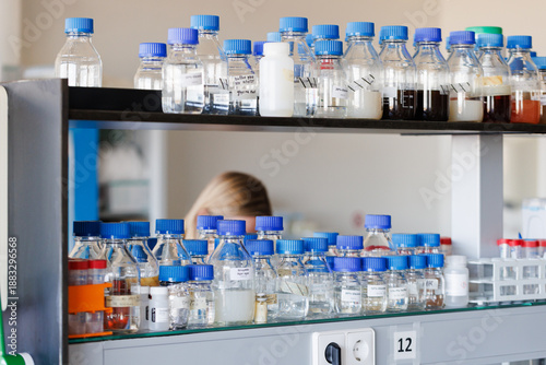 Transparent bottles with blue caps containing different chemical liquids on a shelve in a lab