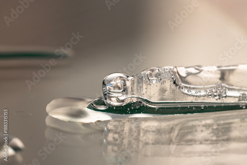 Pipette with transparent liquid, serum, essential oil on beige background, macro.