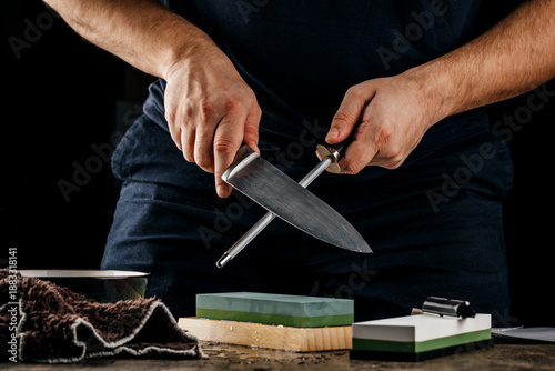 A man sharpens a knife with a grindstone on a rustic wooden table.