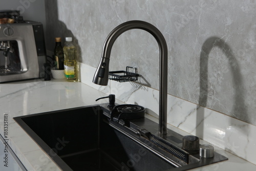 A high-end black undermount kitchen sink is installed in a white marble countertop, featuring several integrated cleaning accessories