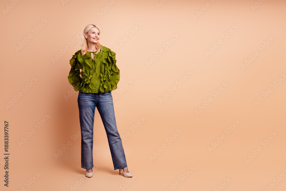 Fototapeta premium Elegant mature woman wearing green ruffled blouse and jeans posing in studio