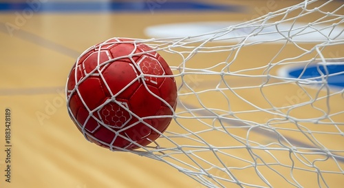 Vibrant Red Handball Caught Firmly in a White Goal Net on an Indoor Court