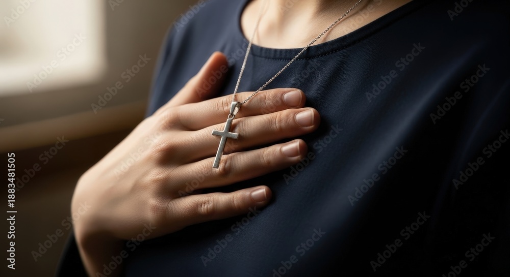 Fototapeta premium Woman in dark shirt holding hand on chest with silver cross necklace. Concept of Christian faith, spirituality, prayer, and devotion