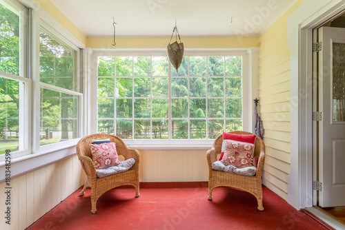 Schilderij op canvas Bright sunroom interior with wicker chairs, large windows, and garden view