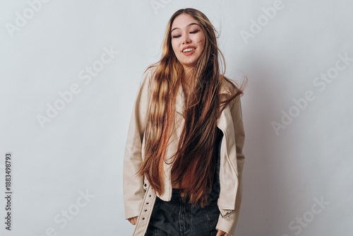 Young woman with long hair wearing casual outfit and light jacket standing against white background with eyes closed and relaxed expression. Female, fashion, portrait, model.