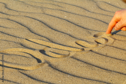 Finger writing message on sand beach, close-up conceptual background
