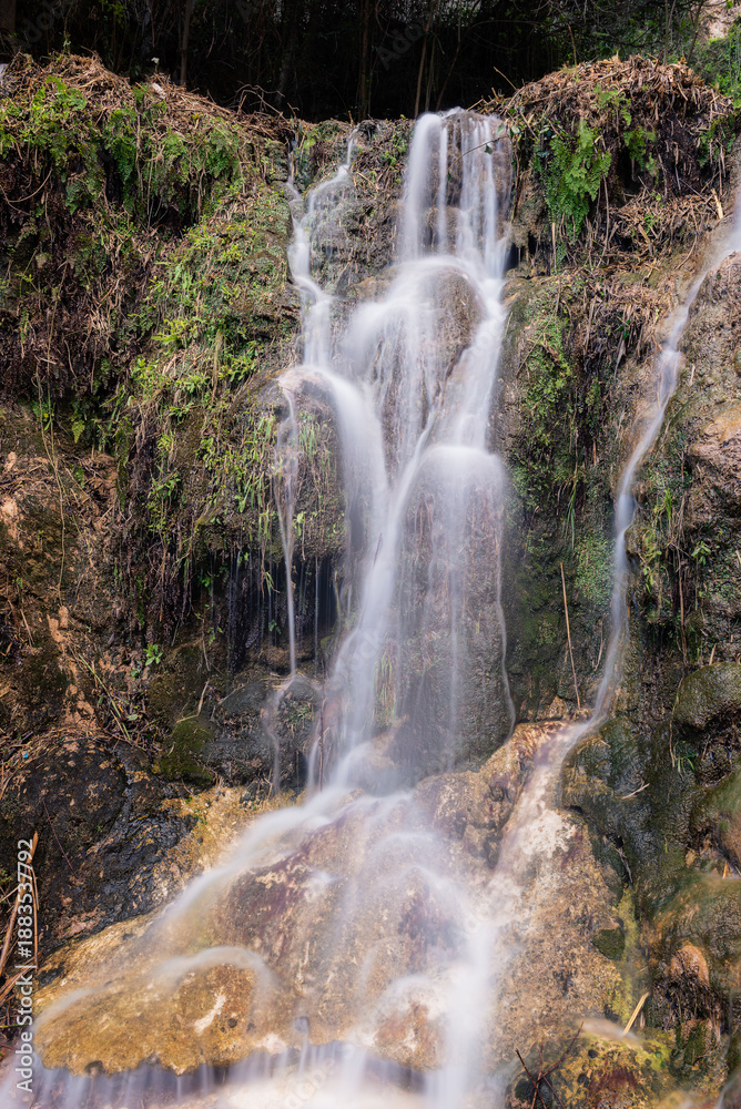 Fototapeta premium Blurred Water Cascading Over Green Mossy Rocks