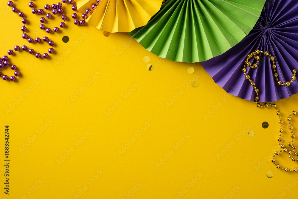 Obraz premium A bright yellow backdrop showcases green and purple paper fans, gold beads, and scattered confetti, capturing a lively Mardi Gras celebration and warm greeting