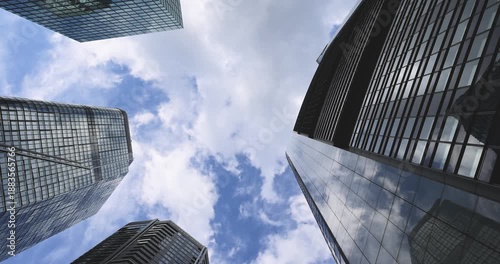 Low-angle view between modern skyscrapers in Frankfurt am Main, looking up at glass and steel office towers against a cloudy blue sky. Contemporary urban architecture in the financial district, convey