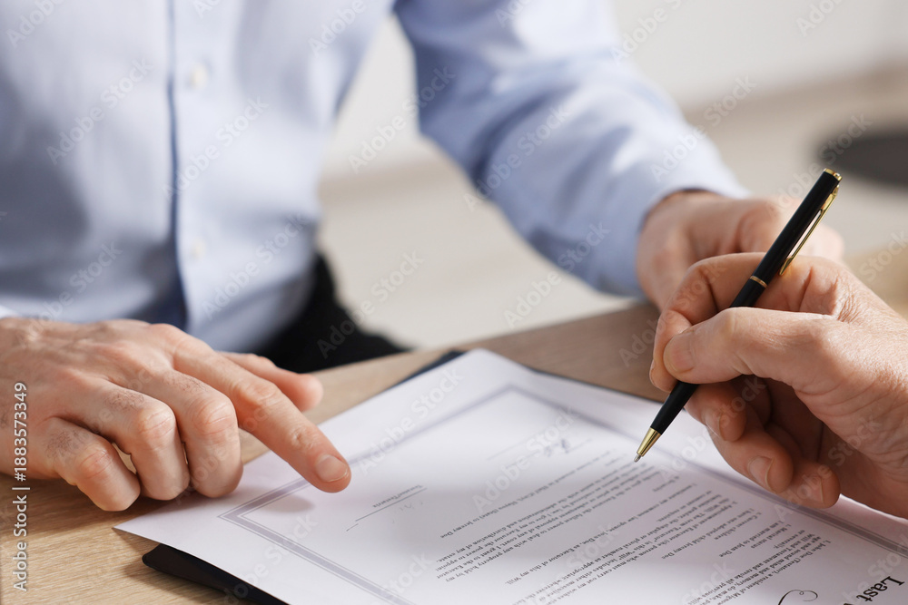 Fototapeta premium Notary showing senior man where to sign Last Will and Testament at wooden desk in office, closeup