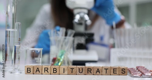 Laboratory specialist studies barbiturates through modern microscope. Wooden cubes on table form word Barbiturates near organized laboratory equipment