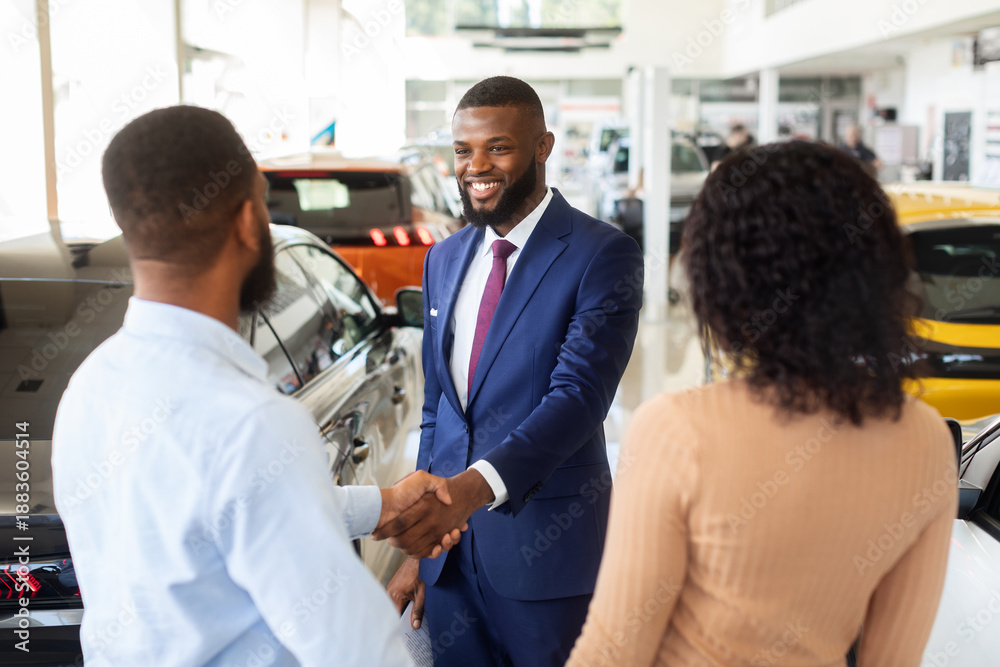 Fototapeta premium Car Dealership Concept. Salesperson Handshaking With Young Black Customers Couple In Showroom, African American Spouses Buying New Automobile In Modern Auto Salon, Selective Focus On Manager