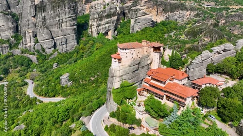 Aerial drone flight towards the Roussanou Monastery (St. Barbara) in Meteora, Greece. View of the convent built on a pillar, with winding roads and massive rock formations