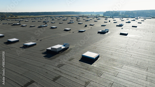 Large industrial flat roof with skylights on modern warehouse building in rural landscape