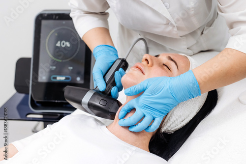 Bild auf Leinwand Female patient receiving microneedle RF treatment on the face in a modern clinic with professional equipment and digital control