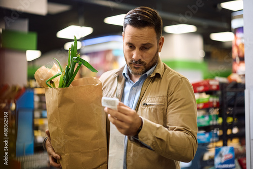 Distraught man looking at grocery prices on bill after shopping in supermarket.