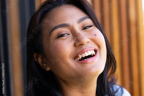 Mid-adult Asian woman laughing, tilting head back in studio, showing earrings against wooden slats