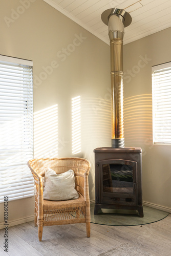 Metal wood stove is sitting on glass hearth pad in corner, armchair and blinds casting stripes