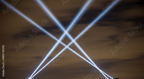 Bright spotlights shining upwards into the night sky during an outdoor event, creating an impressive display of light and energy.
