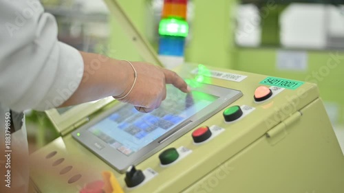 A close-up view of a hand operating a modern industrial control panel with various buttons and a touchscreen display, showcasing technology in manufacturing and production settings
