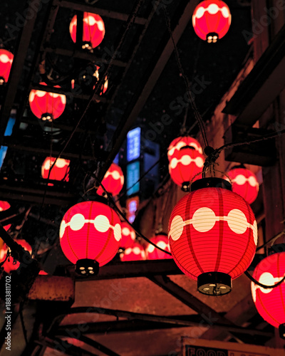 Selective focus on one of many red paper lanterns hanging above a shopping area at night in west Tokyo