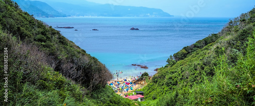 Looking down the valley leading to Kujuppama Beach on Izu peninsula in eastern Japan, with many beach-goers and colorful sun shades visible