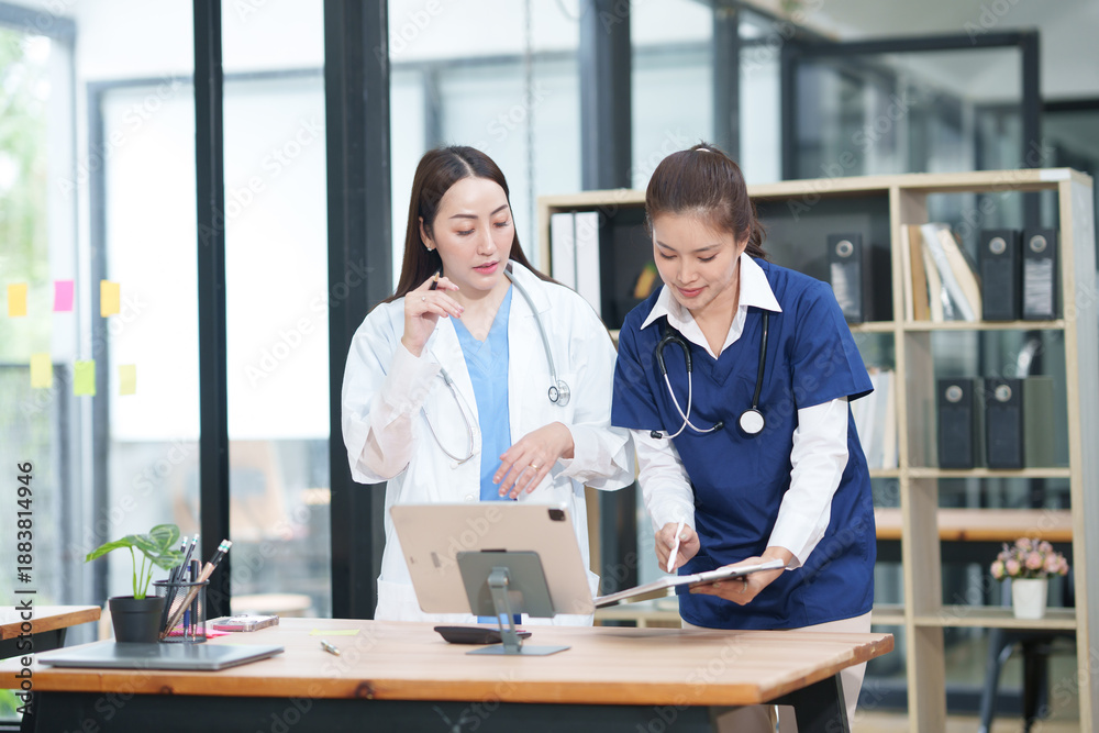 Obraz premium Two female healthcare workers, one in blue scrubs and another in a white lab coat, are collaborating and reviewing patient charts on a clipboard and tablet. They are engaged in a professional discussi